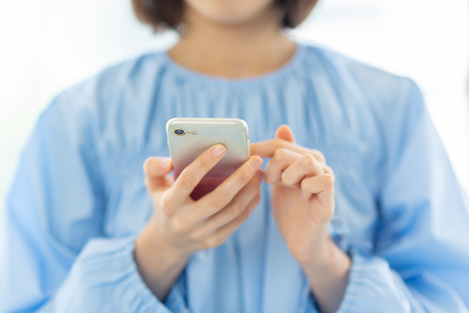 ブルーのブラウスを着た女性がスマートフォンで市民葬祭アステルに連絡を取る想定の場面、宇都宮市 葬儀の問い合わせを示す緊急対応イメージ